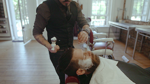 Barber applying shaving cream to client beard