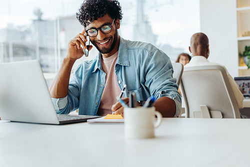 Young businessman smiling while speaking on smartphone at modern office
