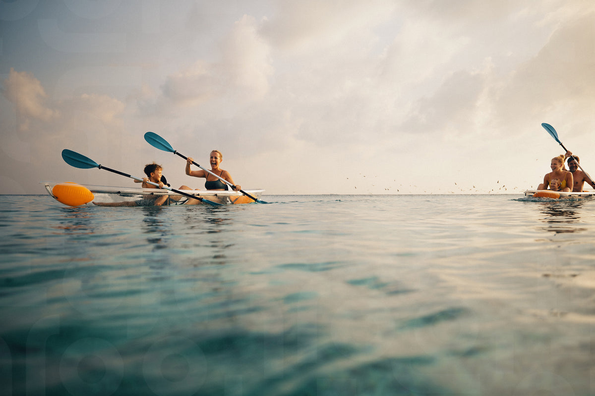 Adults and children kayaking in clear ocean waters under a sunny sky ...