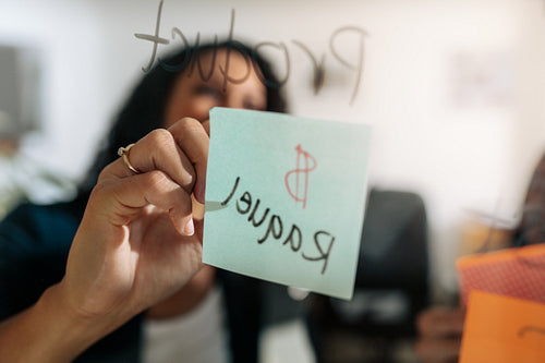 Businesswoman writing on a sticky note pasted on a glass board in office