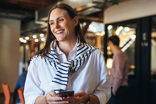 Happy business woman holding a cellphone in a workplace