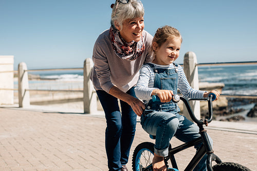 Senior woman helping her granddaughter learn to ride a bicycle