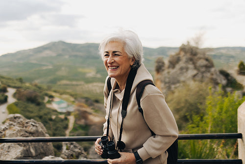 Cheerful senior woman using binoculars while hiking