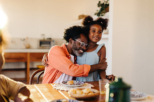 Mature dad hugging his young daughter at the breakfast table before a pão de queijo meal