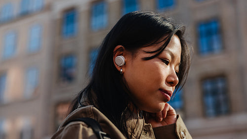 Woman listening with earbuds in thoughtful urban portrait