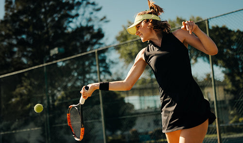 Young woman playing tennis, hitting ball near fence