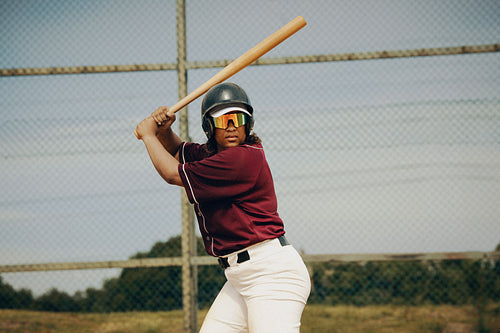 Confident female baseball batter wearing sunglasses prepares for a powerful swing