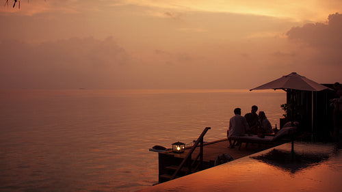 Luxury resort guests gather on a private overwater deck watching the sunset