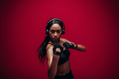 Young woman in sportswear boxing on red background