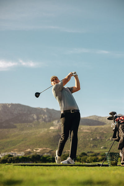 Man taking a golf shot in action on a sunny day with mountains in the background