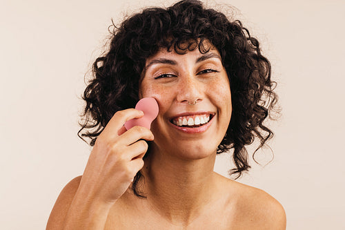 Cheerful woman using a makeup sponge on her face