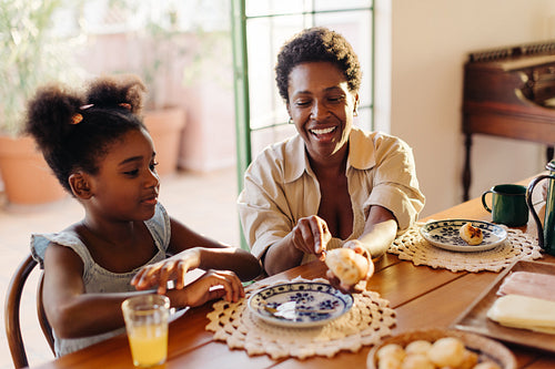 Brazilian mom cutting on a cheese bread roll for her daughter during breakfast