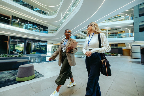 Two female colleagues walking and chatting in modern office space
