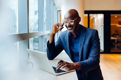 Man in formal suit using a laptop while having a phone conversation