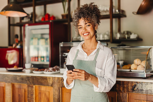 Successful cafe owner holding a smartphone in her cafe