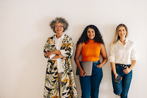 Three diverse businesswomen standing against an office wall