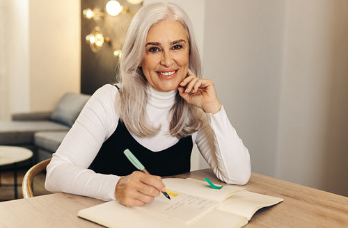 Productive senior woman writing in her diary at her home office