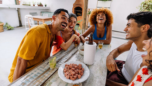 Group of five friends laughing while sharing petiscos on a patio
