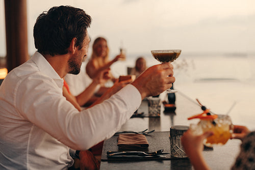 Group of friends enjoying a sunset dinner with drinks at a beachfront venue