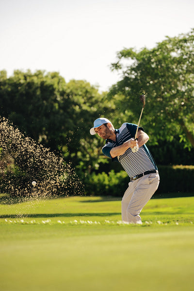 Action shot of a male golfer chipping the ball onto the green from a sandy bunker
