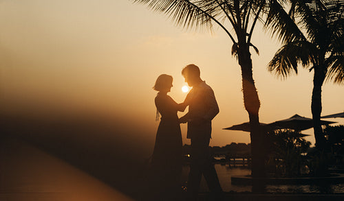 Romantic couple silhouette dancing in the sunset under palm trees