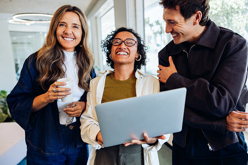 Three coworkers share a laptop and laughs
