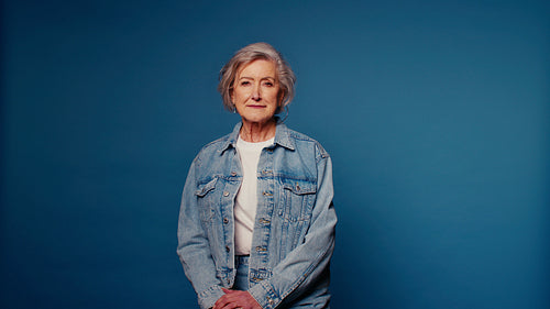 Confident senior woman in denim jacket on blue background