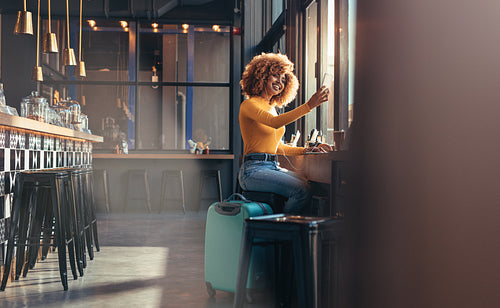 Smiling female traveller sitting at a coffee shop with her luggage