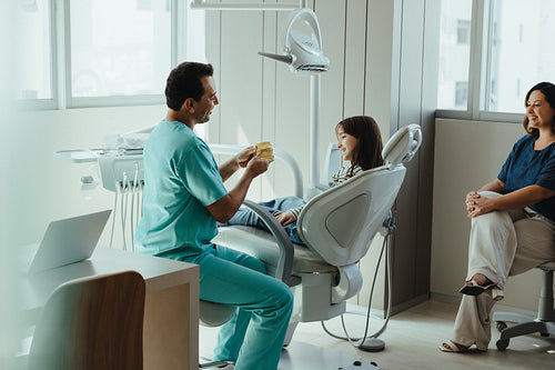 Dentist explaining dental care to child patient during family clinic checkup