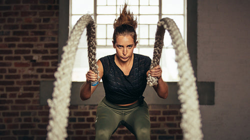 Sportswoman exercising with battling ropes at gym
