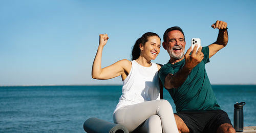 Senior couple taking a joyful selfie by the ocean during fitness activities