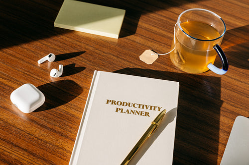 The desk scene with a planner, earbuds, and sticky note supports focused work