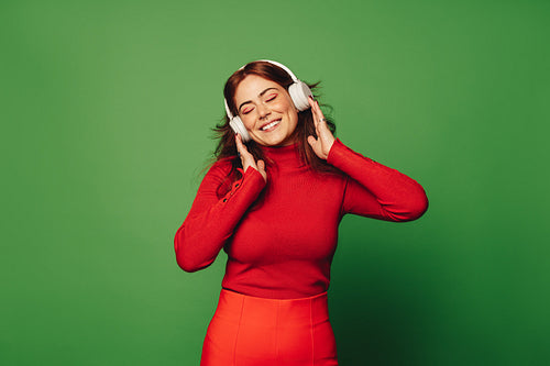 Happy woman enjoying festive holiday vibes and vibrant music on wireless headphones