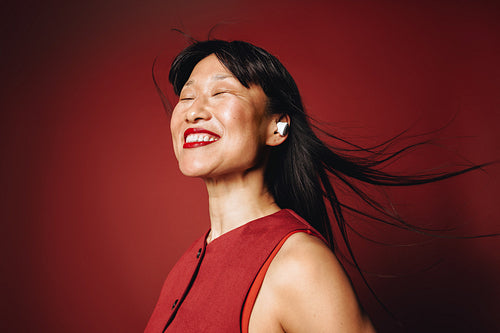 Smiling woman with earbuds enjoys audio in a red studio portrait