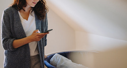 Mother standing by baby crib using cell phone