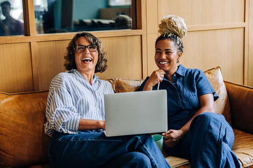 Two women smiling and working on a laptop in a cozy office setting