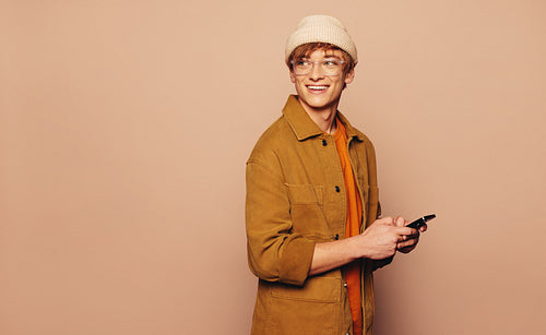 Cheerful young man using smartphone against vibrant peach background