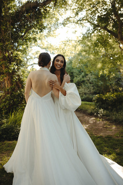 Two brides embracing outdoors in wedding dresses during a daytime ceremony