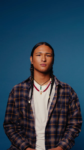 Calm young indigenous man in plaid shirt on blue background vertical portrait
