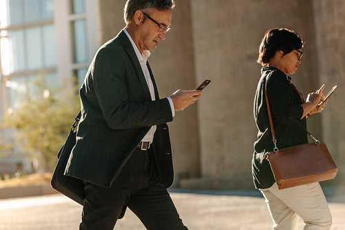 Business people busy using mobile phone while walking on street to office