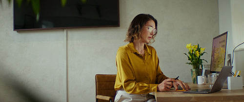 Businesswoman typing on laptop, reviewing marketing strategy on desktop, medium shot