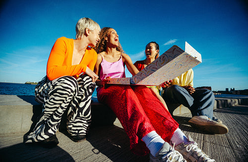Sharing pizza, friends gather by the waterfront on a sunny day