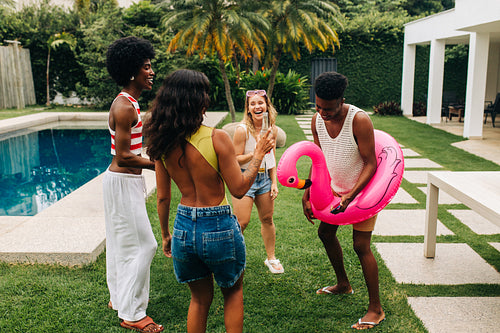Friends enjoy pool party outdoors with inflatable flamingo and drinks