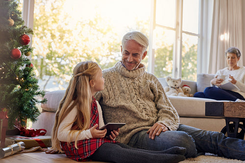Little girl and grandfather by christmas tree with tablet pc