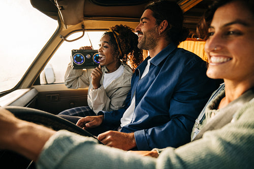 Friends enjoying a road trip in a car with a boombox and smiles