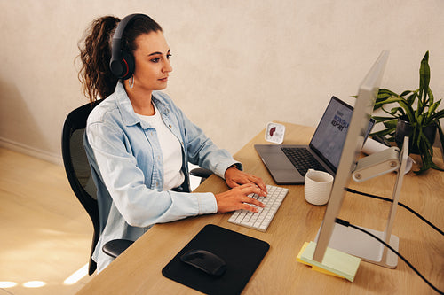 Woman working at desk in office wearing headphones, staying focused and productive