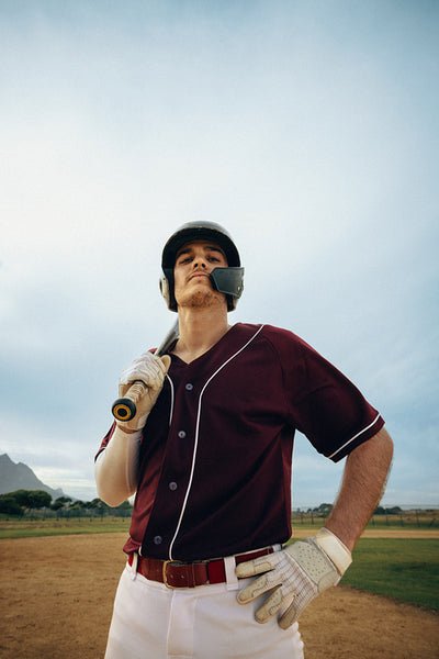 Confident male baseball batter standing on the field holding bat, ready for the competition