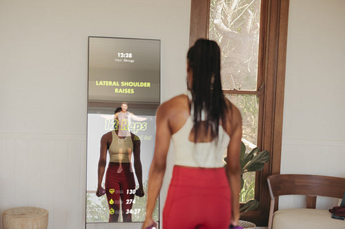 Young woman using a smart fitness mirror for virtual workout class