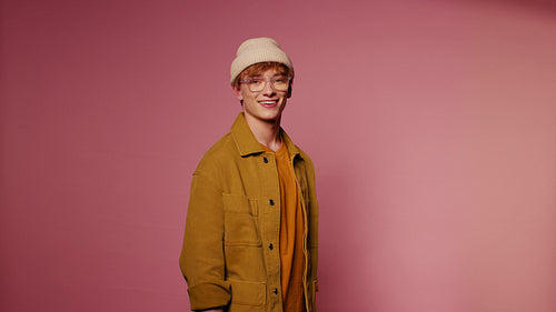 Young stylish man smiles against a pink background in a medium shot
