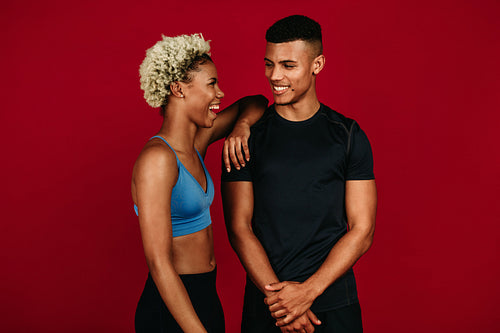 Cheerful fitness couple standing together on maroon background